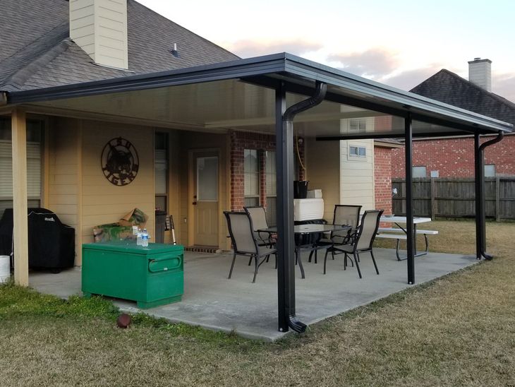 Covered patio with black metal furniture, green storage box, and brick house exterior at dusk