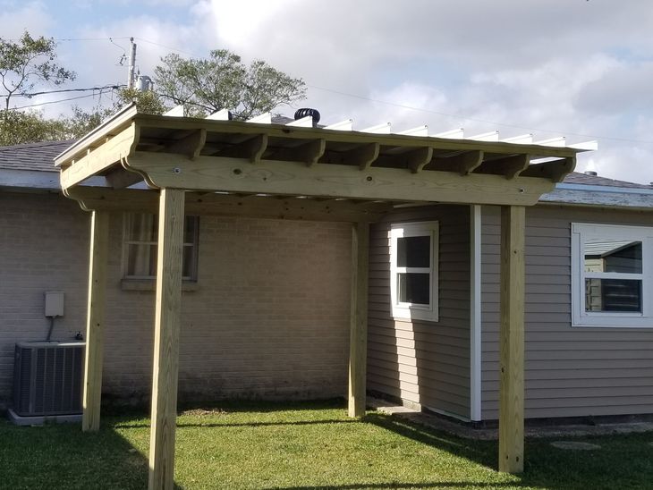Small wooden patio cover attached to a house, with two posts over a grassy yard.
