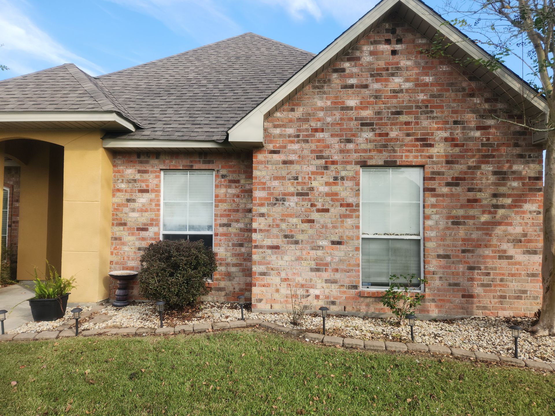 Brick house front exterior with two windows, a gabled roof, and a grassy yard