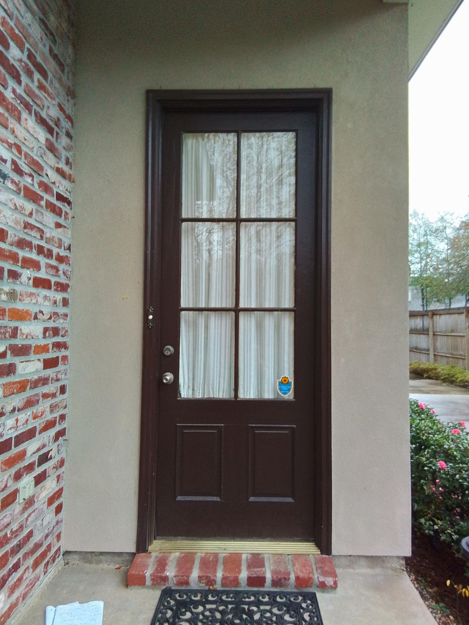 Front entry door with dark wood, glass panel, and brick step beneath a covered porch
