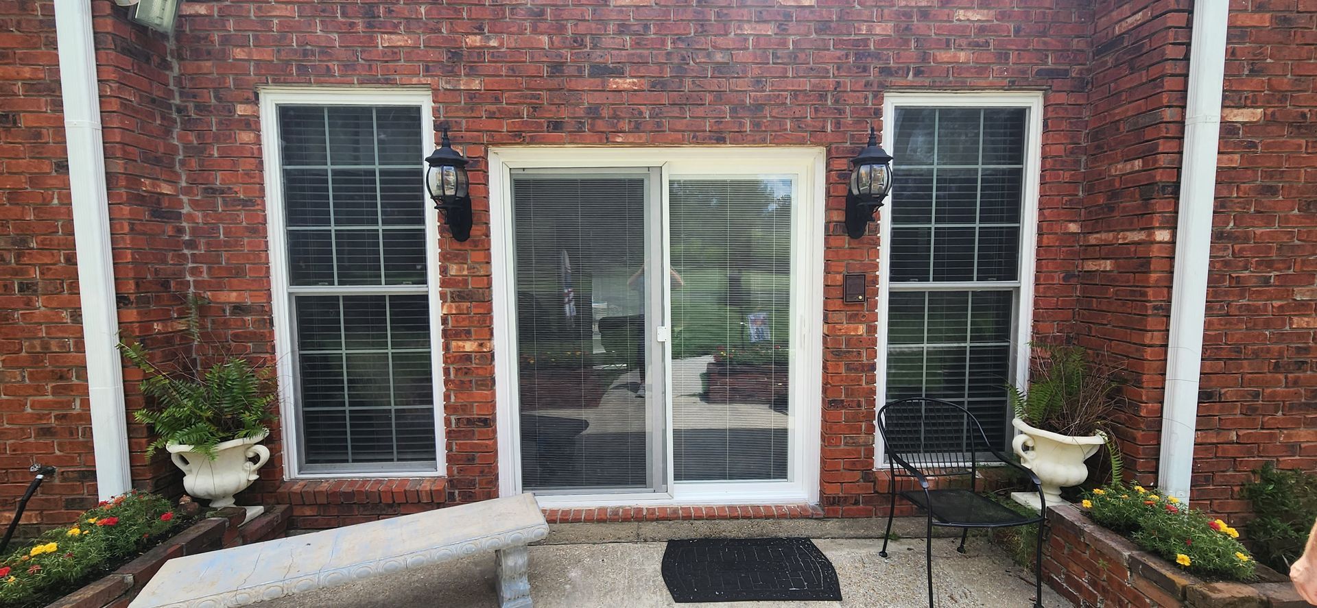 Brick house entry with white French doors, black shutters, and potted plants on either side