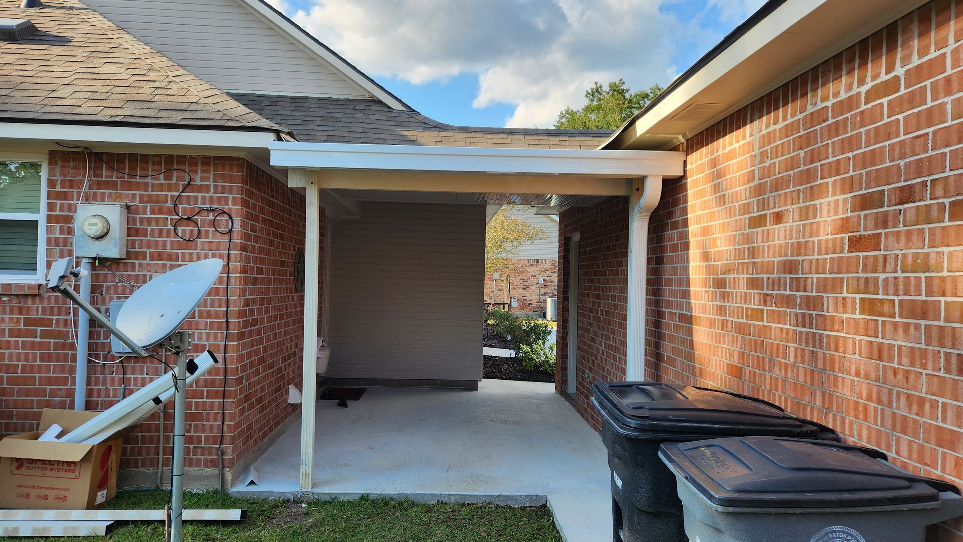 Backyard alley between brick houses with a satellite dish, walkway, and trash bins