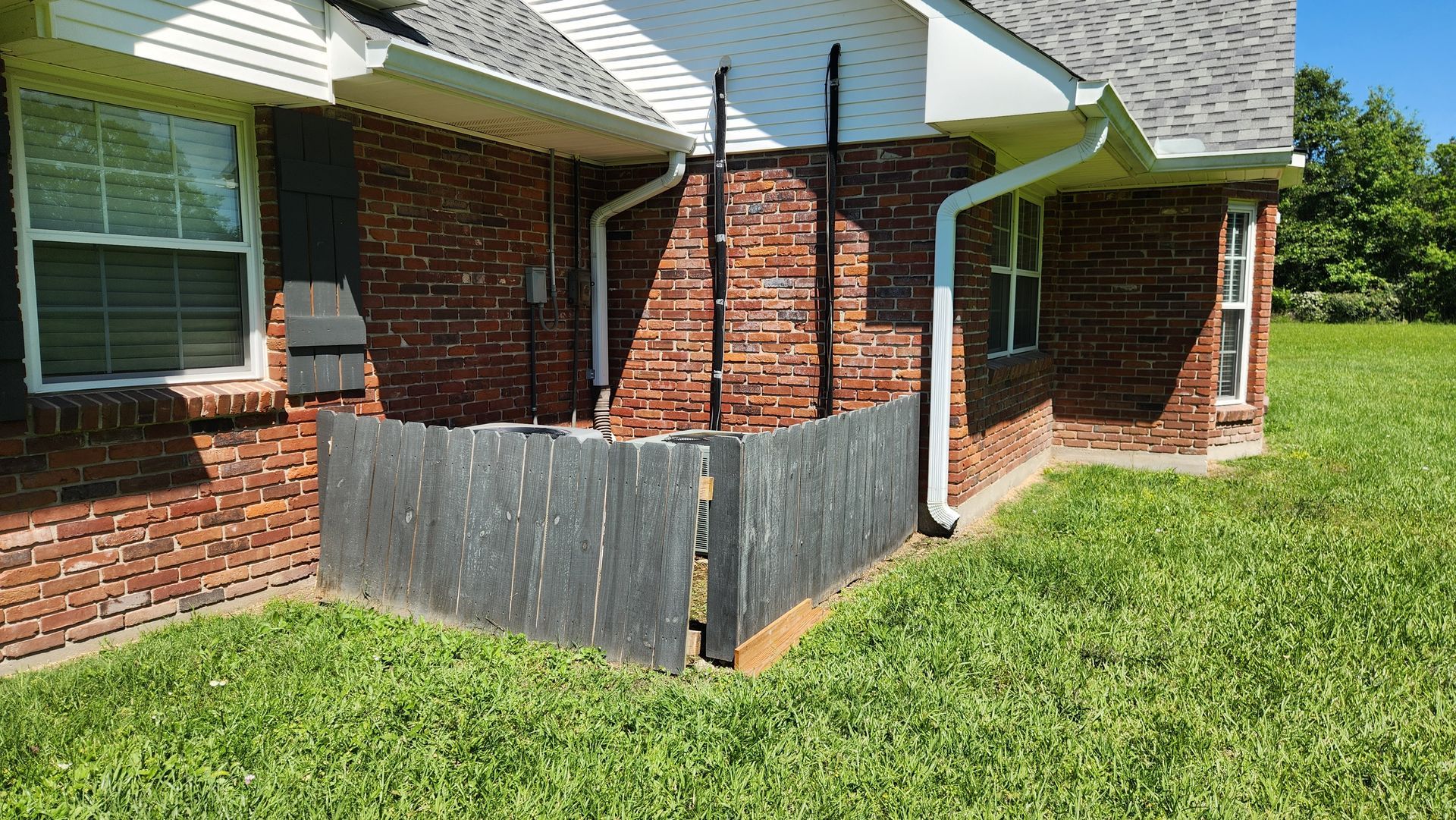 Brick house patio with a wooden privacy fence and grassy yard under a bright sky