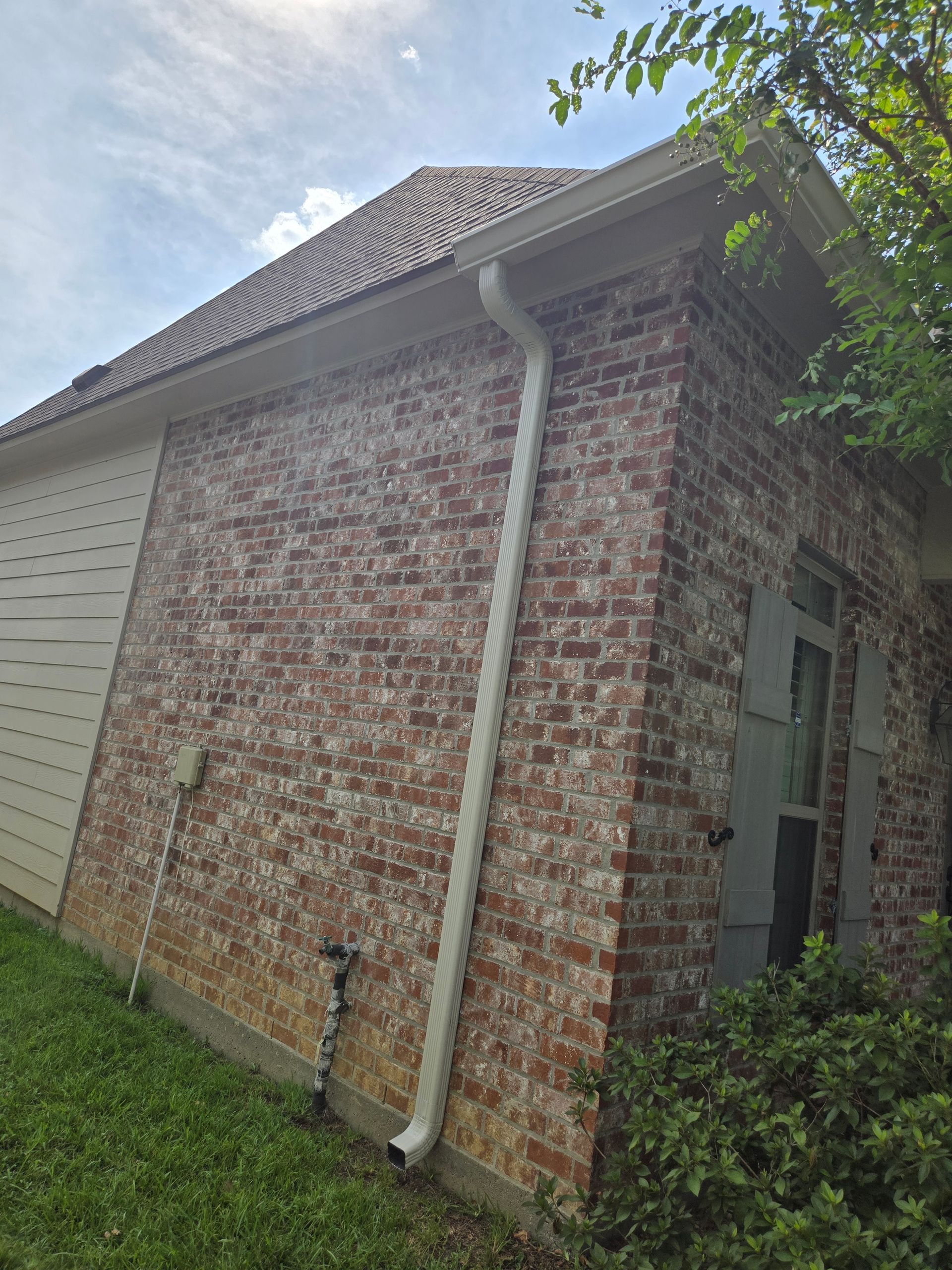 Brick house exterior with white gutter, gray roof, and white siding in sunlight