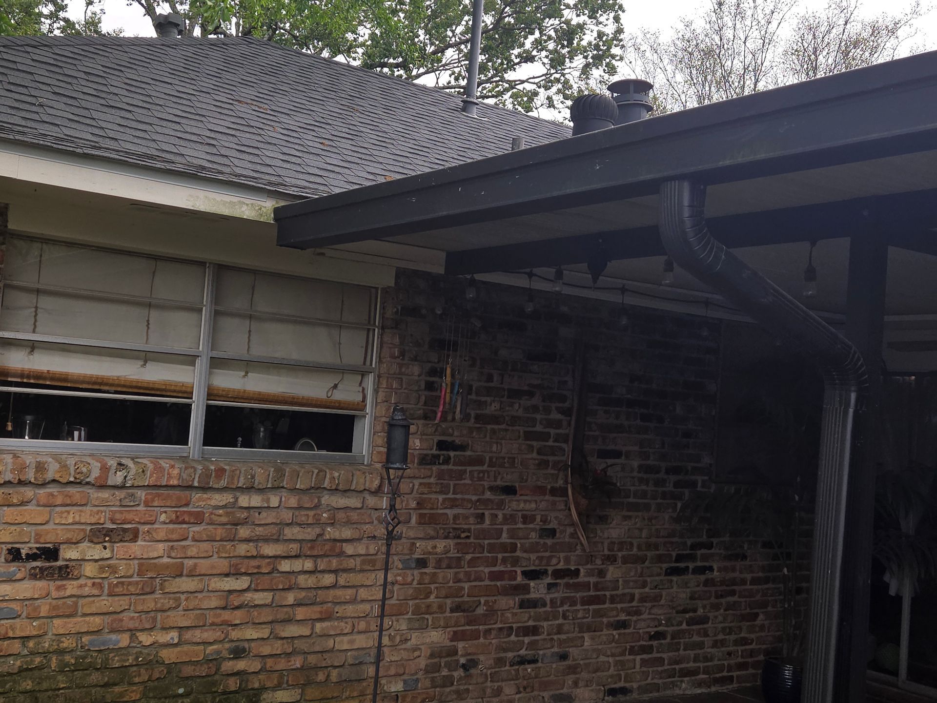 Damaged brick house exterior with broken window and dark roof overhang