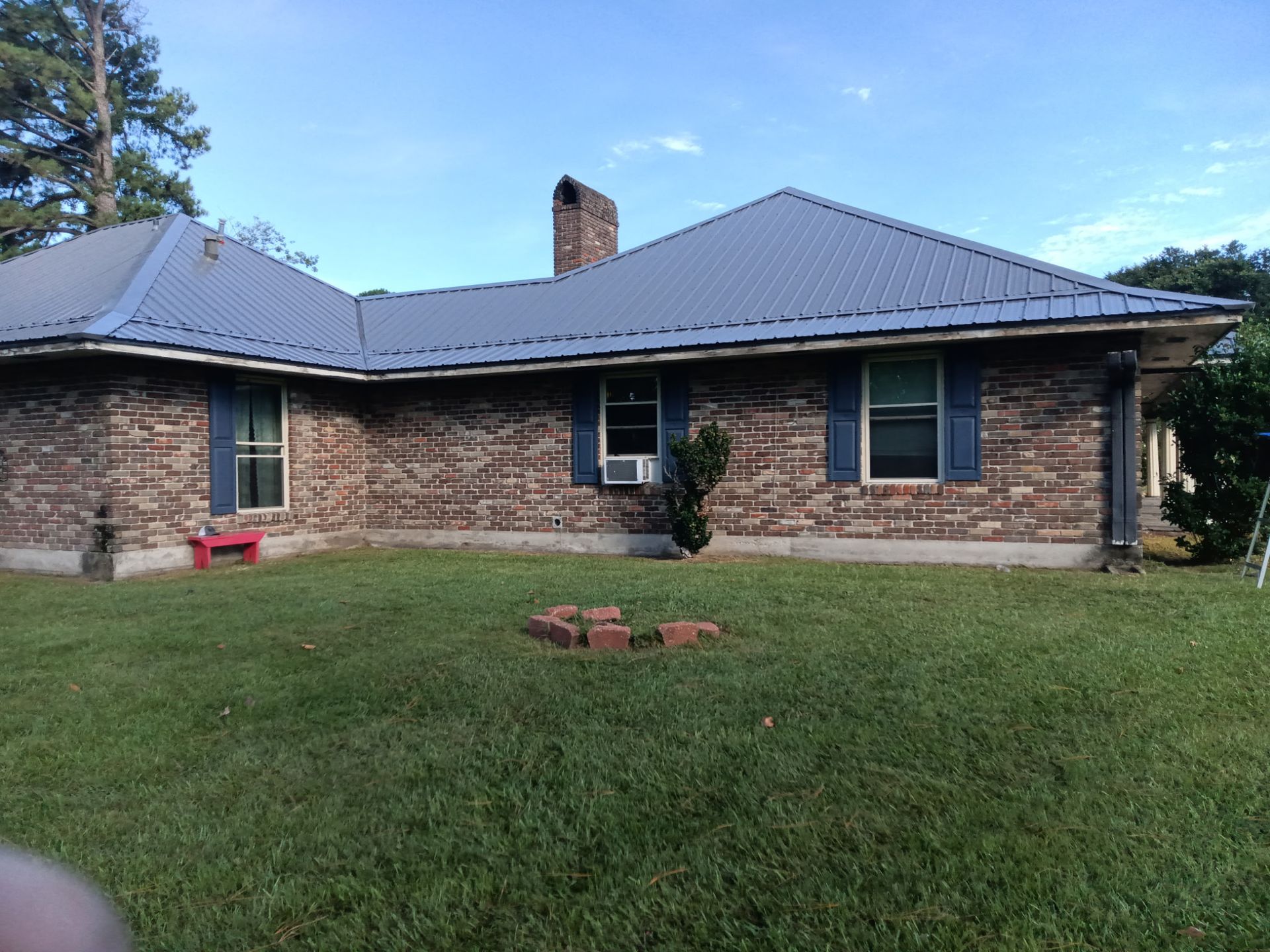 Single-story brick house with gray roof and chimney, seen from a grassy front yard.