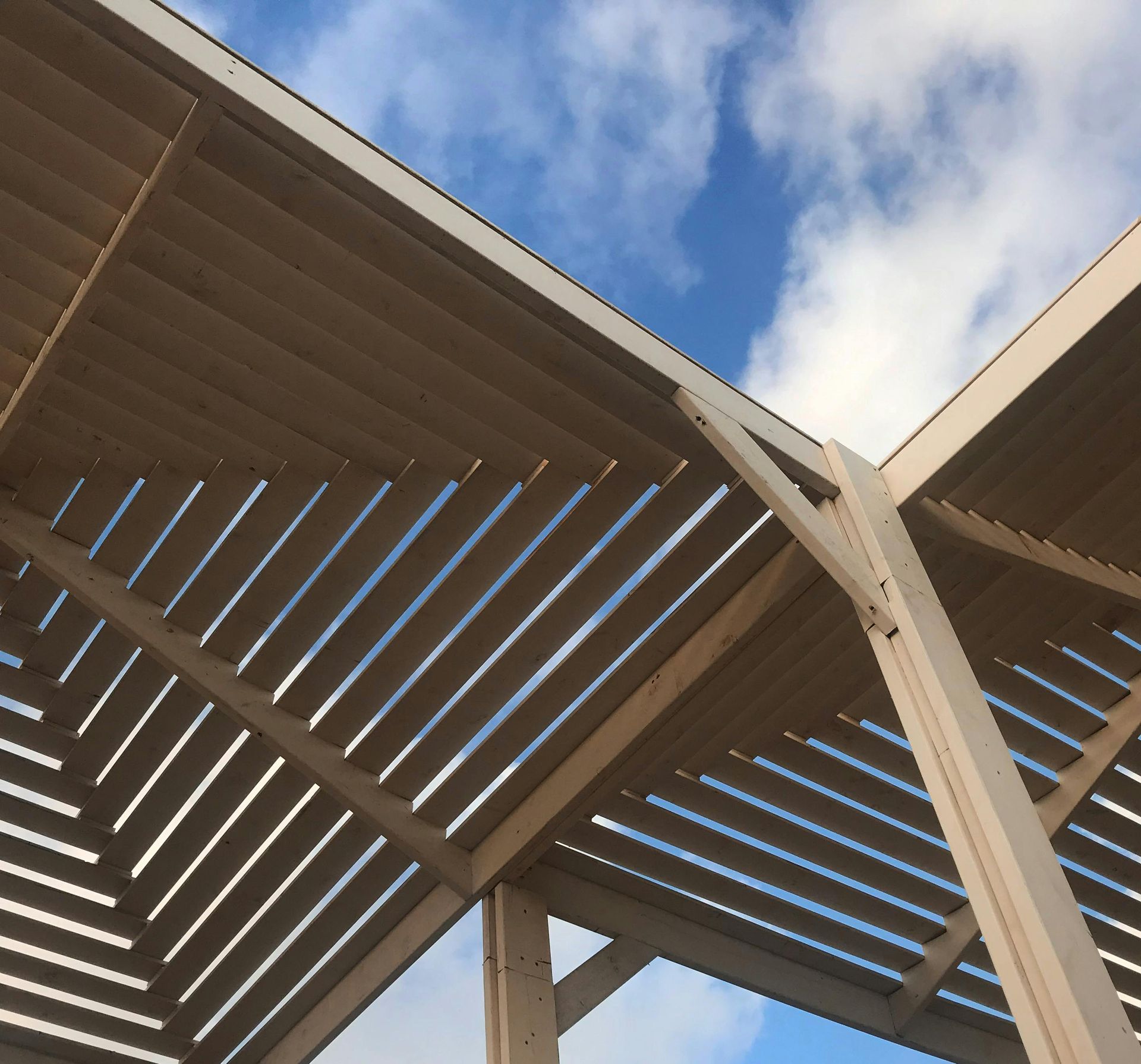 Wooden slatted pergola roof against a blue sky with clouds