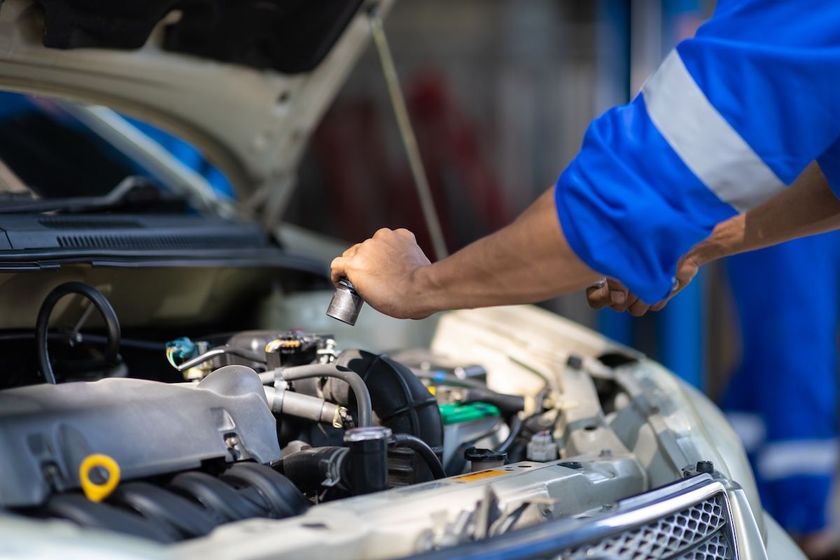 Mechanic in blue uniform inspecting a car engine with the hood open