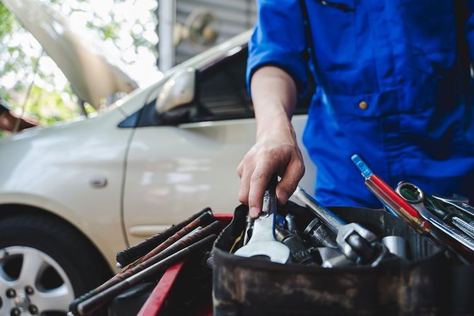 Mechanic in blue coveralls working beside a white car with tools in a bucket