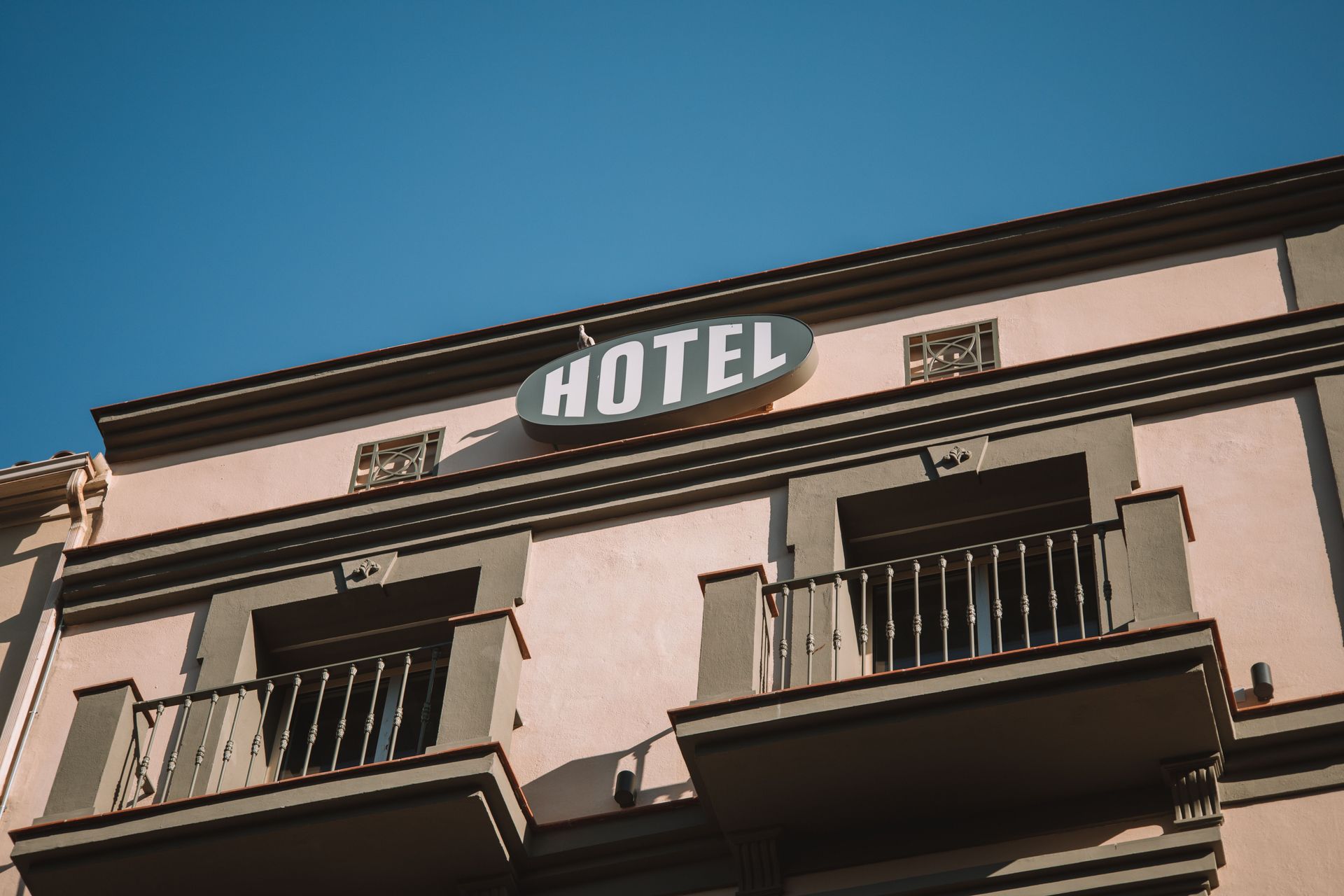 Großes Hotel-Schild an der Außenfassade eines Gebäudes mit Balkonen vor blauem Himmel.