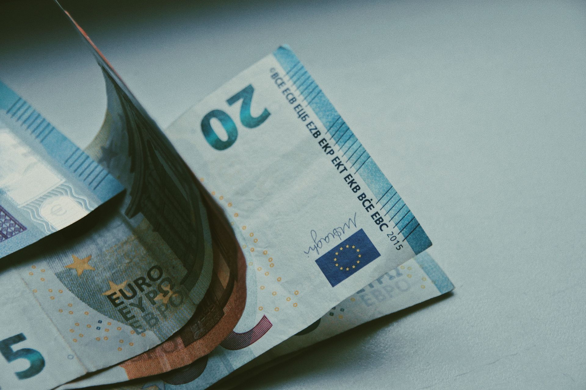 Mehrere ineinandergesteckte Euro-Geldscheine, darunter ein 20- und ein 5-Euro-Schein, auf einer hell