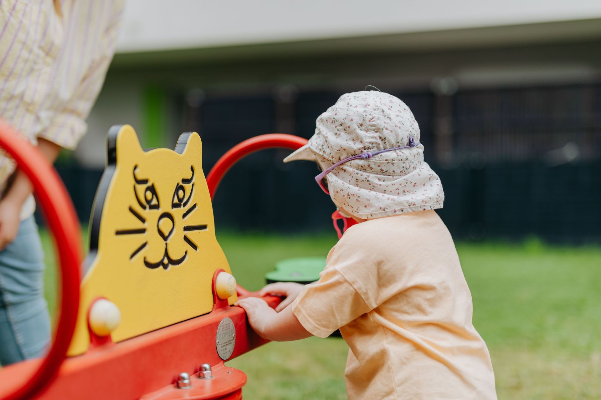 Kleinkind mit Sonnenhut spielt draußen an einem Spielgerät