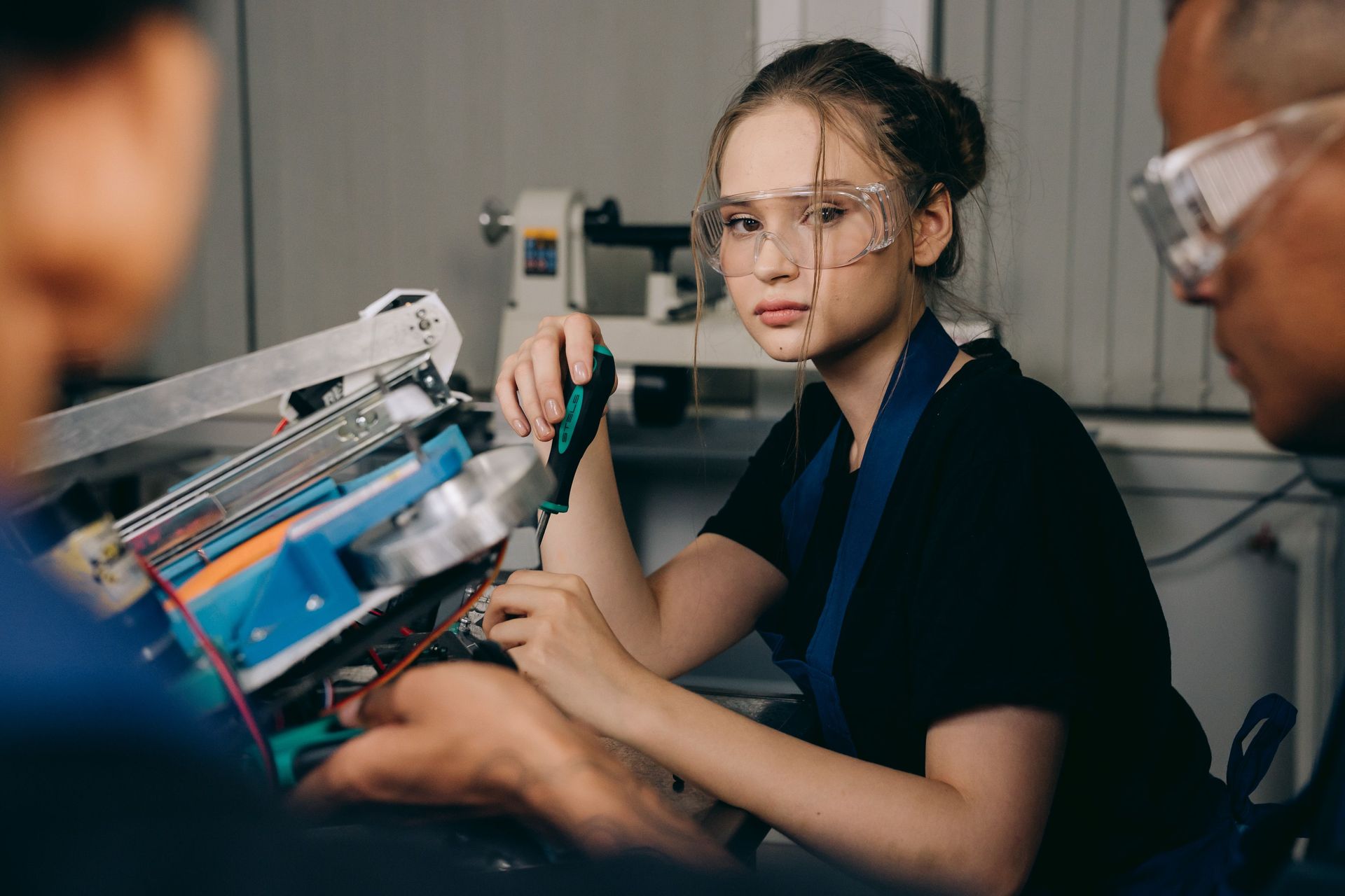 Junge Auszubildende mit Schutzbrille und Schraubenzieher arbeitet an einem technischen Gerät.