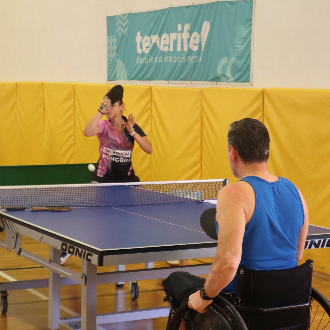 Ein Mann im Rollstuhl spielt Tischtennis vor einem Schild mit der Aufschrift „Teneriffa“