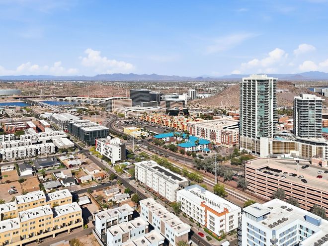 Aerial view of a coastal city with apartment towers, low-rise buildings, and mountains in the distance.