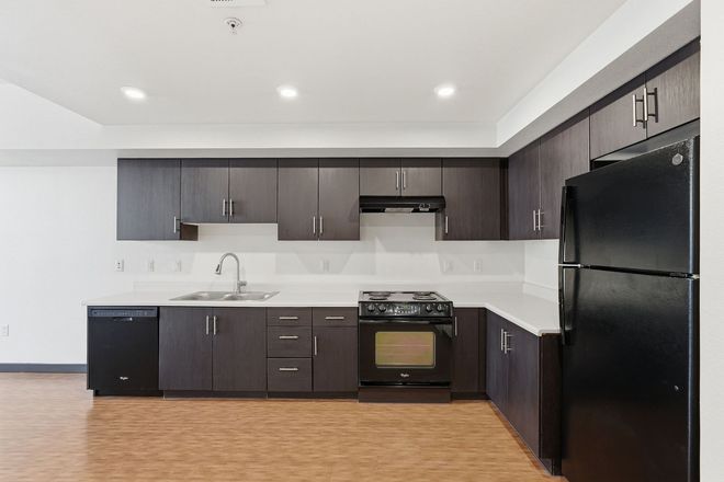 Modern kitchen with dark cabinets, white countertops, wood floor, and black appliances