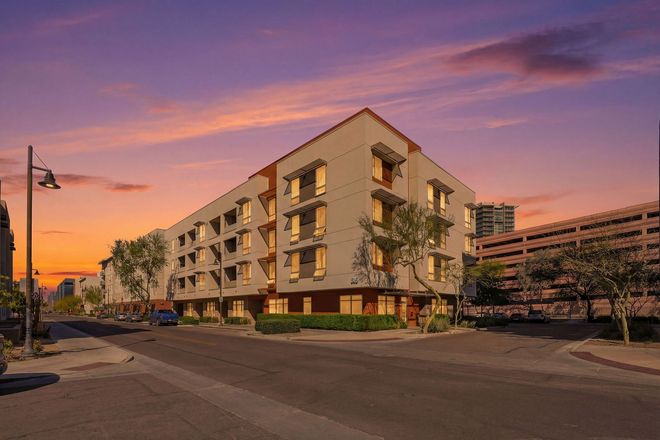 Sunset over a modern apartment building on a quiet street, with pink-purple sky and city lights.