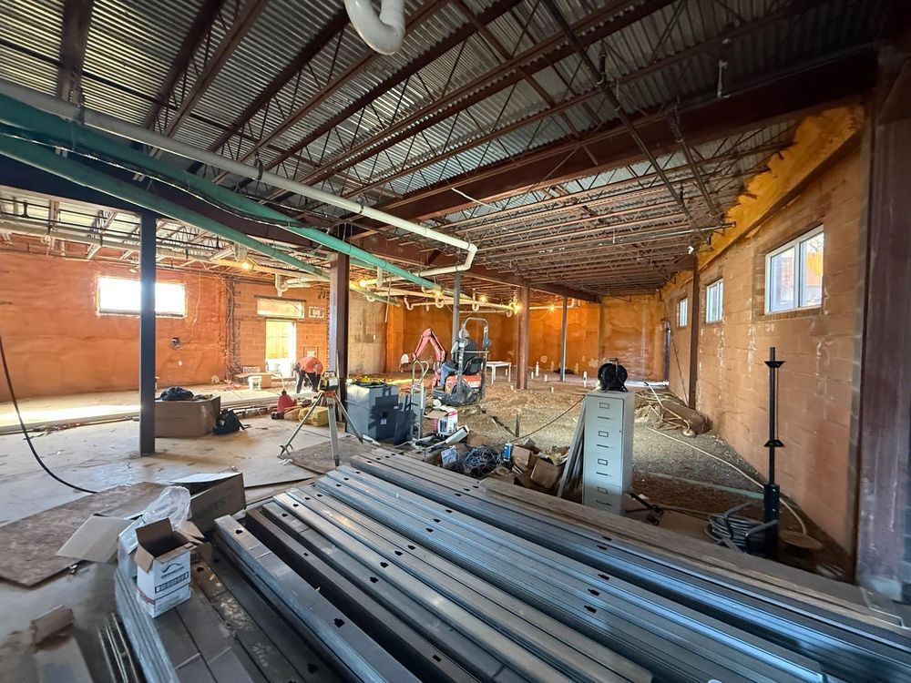 Large unfinished warehouse interior with metal beams, stacked pipes, and construction equipment on the floor