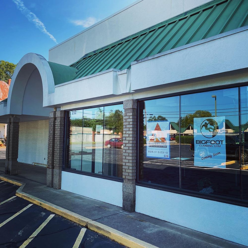 Exterior of a storefront with teal awning, arched entrance, and reflective windows along a parking lot.