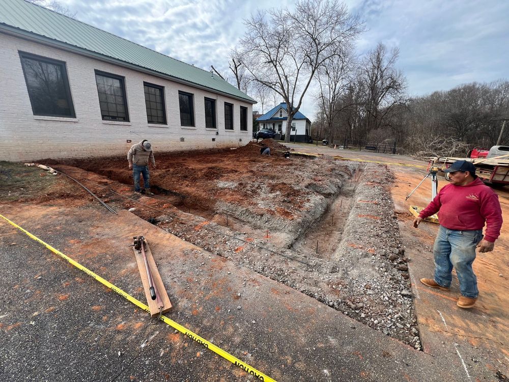 Construction workers excavating a trench beside a white building with windows and a green roof