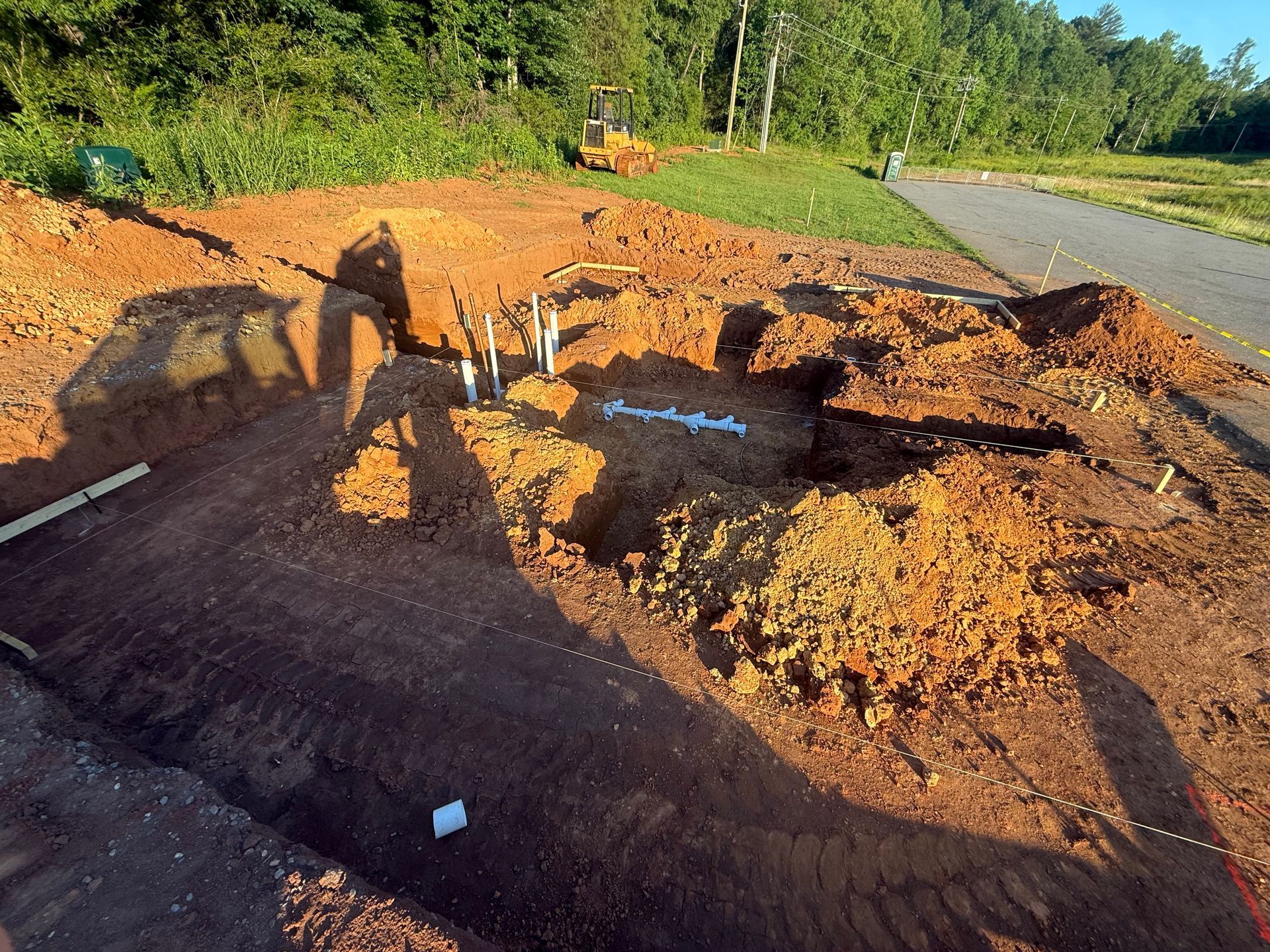 Collapsed road near a roadside ditch with exposed soil and heavy equipment shadows in bright sunlight