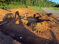 Collapsed road near a roadside ditch with exposed soil and heavy equipment shadows in bright sunlight