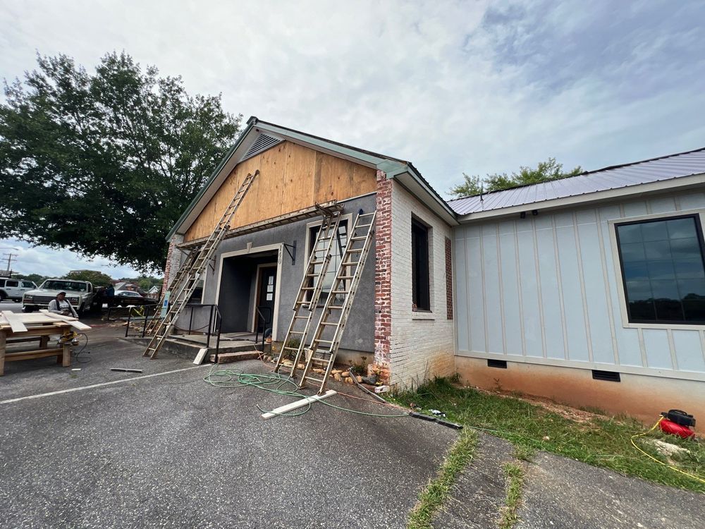 Exterior of a building under renovation with exposed framing, ladders, and a paved driveway.