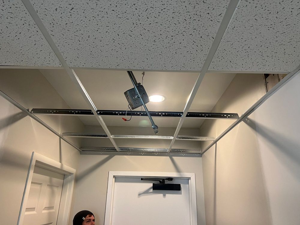 Hallway ceiling with a hanging light fixture and open ceiling tiles, viewed from below