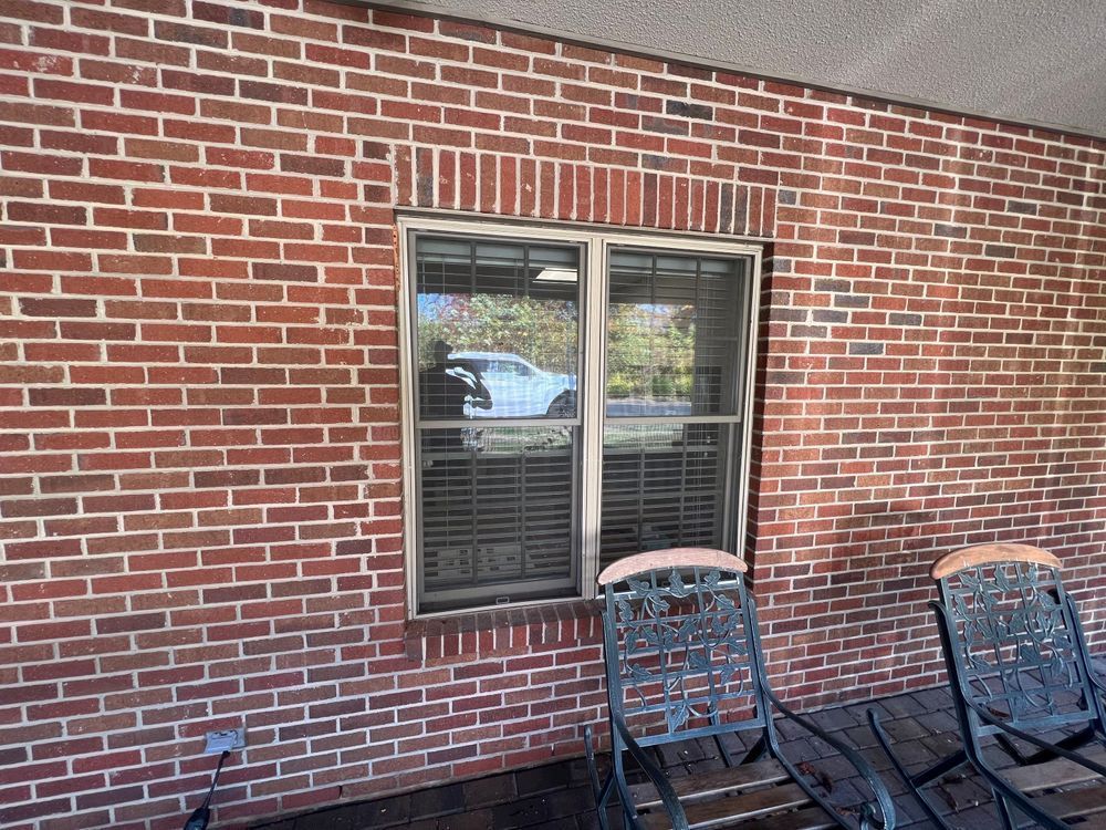 Brick exterior wall with window and two patio chairs on a small paved area
