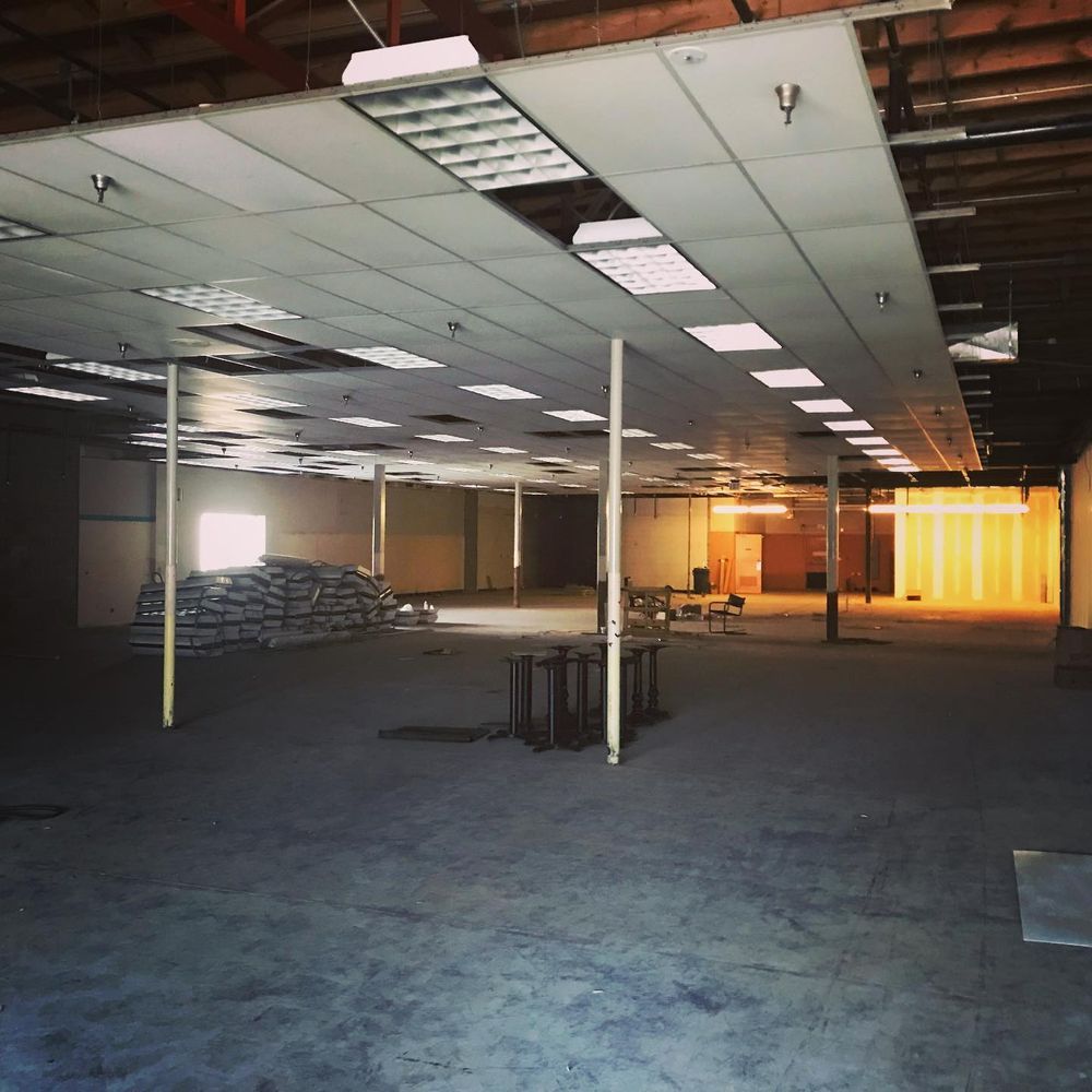 Empty office space with drop ceiling, carpet, support columns, and stacked materials near bright windows