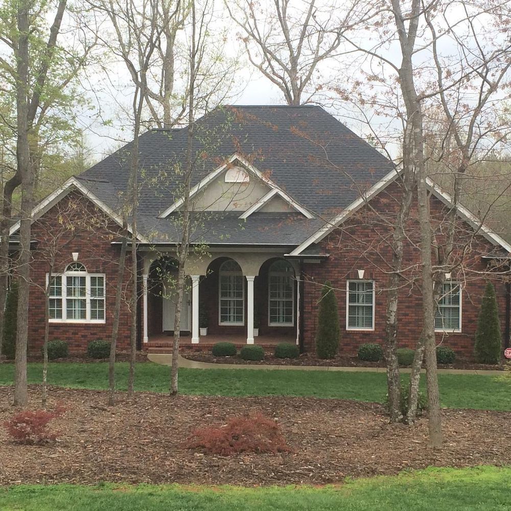Brick suburban house with dark shingle roof, white trim, and trees in the front yard