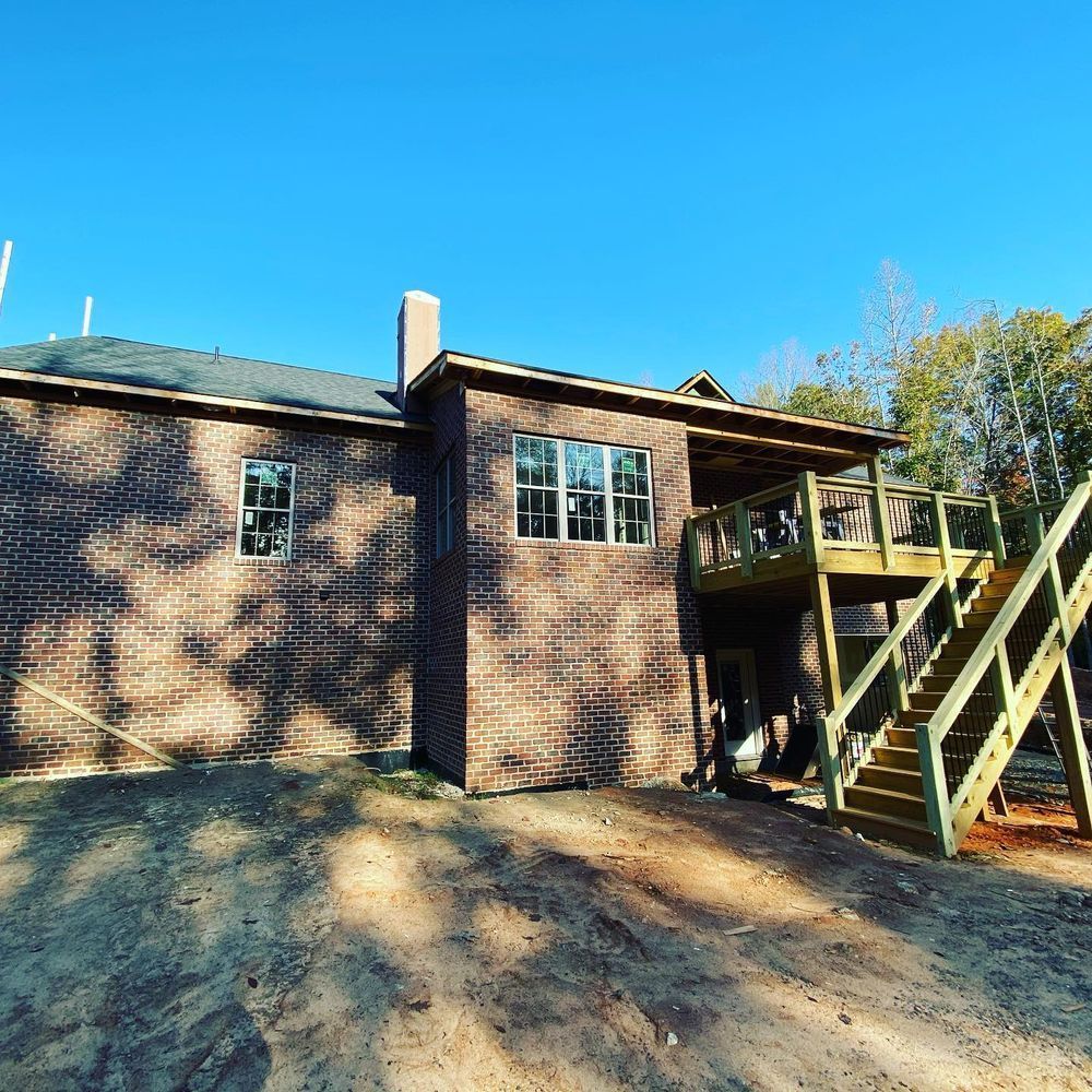 Brick house exterior with deck stairs, windows, and a dirt yard under a clear blue sky