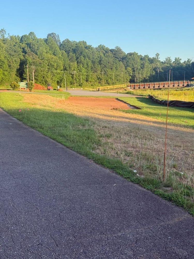 Paved path beside a grassy field and wooded hillside in warm evening light