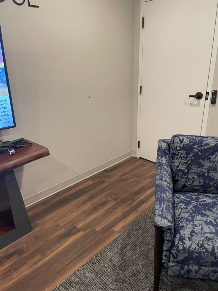 Living room corner with wood floor, gray wall, white door, and blue patterned armchair beside a TV stand.
