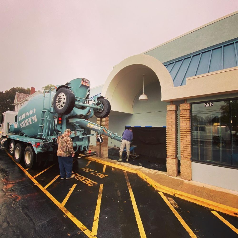 Workers loading a teal cement truck into a building entrance under a covered awning