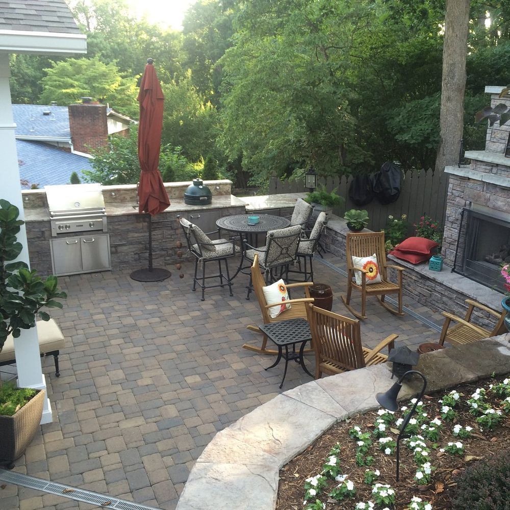 Patio with grill, table, chairs, fire pit, and umbrella beside a garden and stone steps