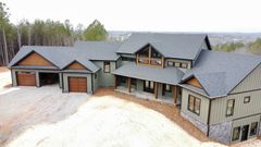Large modern house with gray roof, stone accents, and three-car garage, viewed from above in a snowy setting