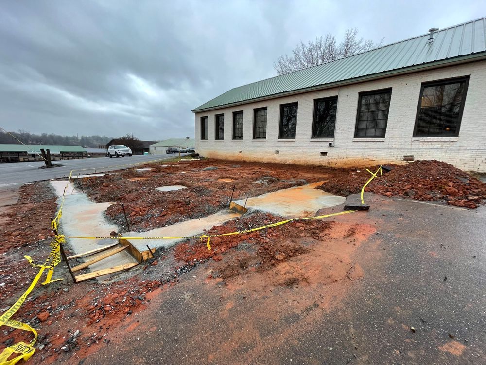 Flooded pavement beside a white building, with broken asphalt and yellow caution tape under gray skies