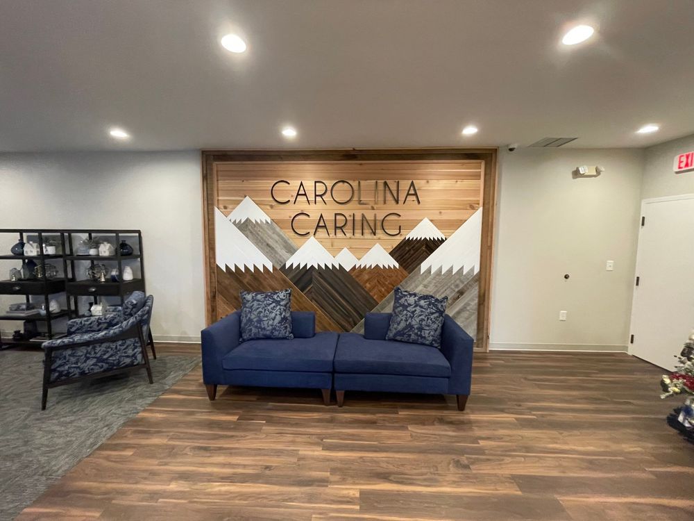 Lobby seating area with blue sofa, wood accent wall, and “Carolina Caring” sign