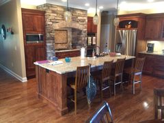 Modern kitchen with stone fireplace, wood cabinets, island, and stainless steel refrigerator