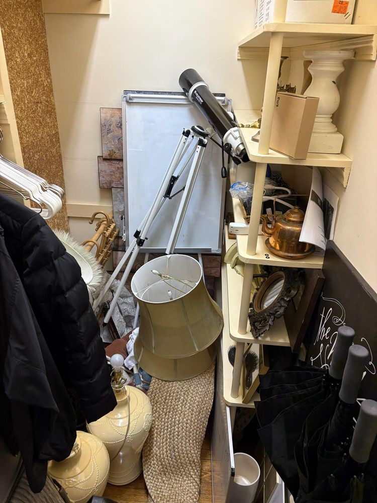 Cluttered closet with vacuum cleaner, lamp, coats, shelving, and household items tightly packed together