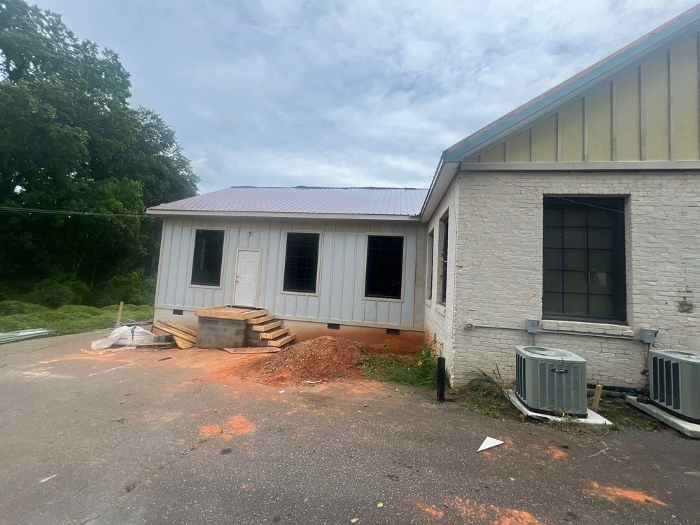 Partially renovated house exterior with white siding, exposed dirt, and window AC units