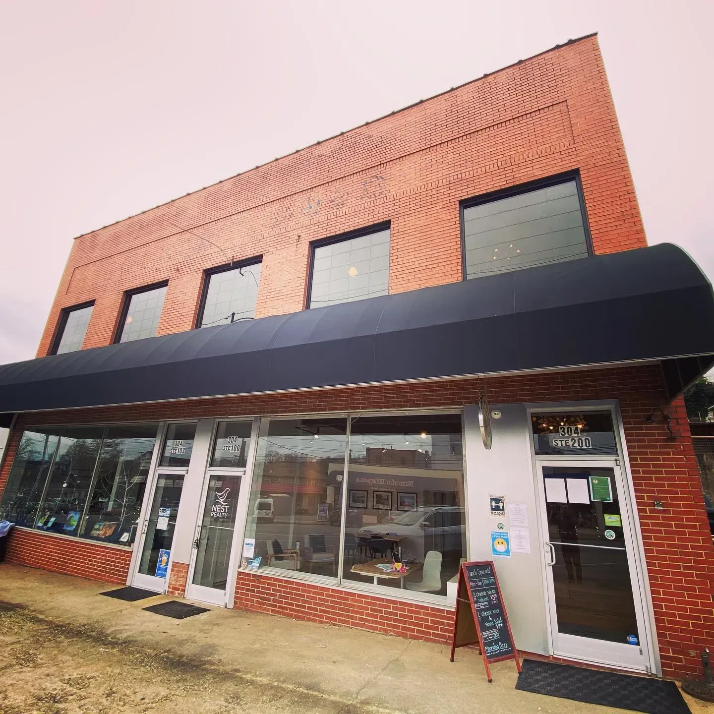 Brick storefront with large black awning, glass windows, and a white door on a cloudy day