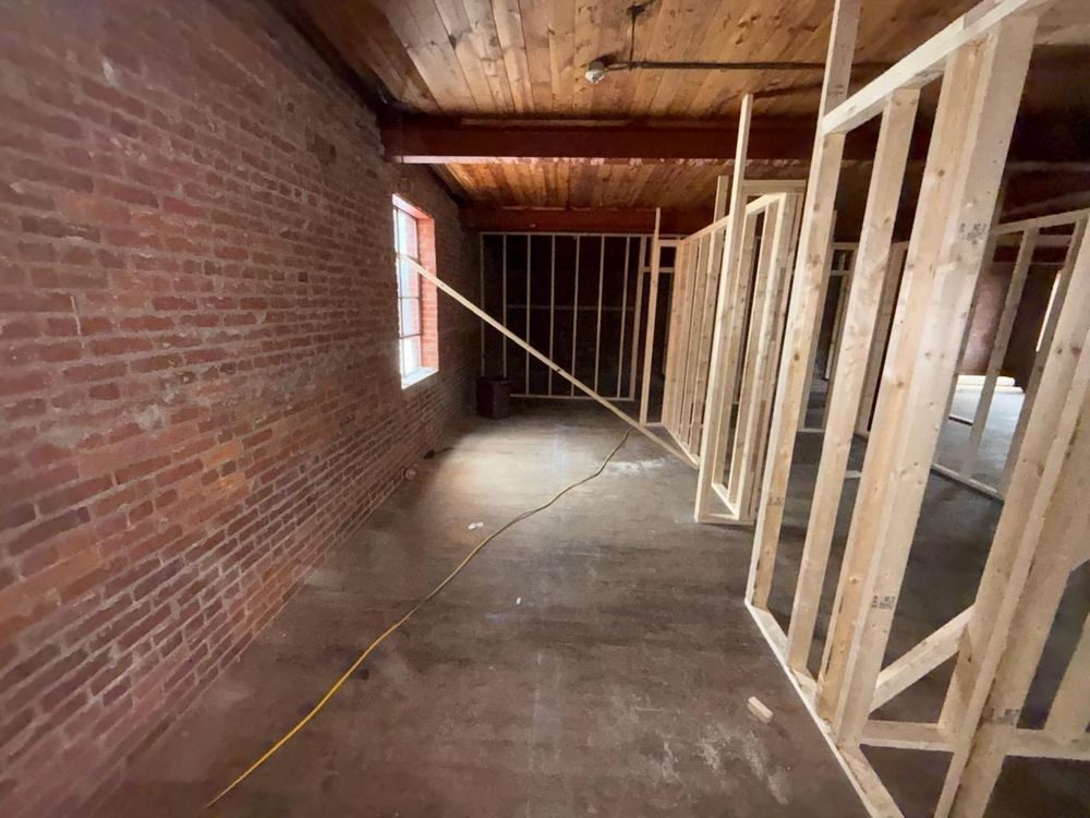 Interior framing of a narrow unfinished room with exposed brick walls, wooden studs, and a concrete floor.
