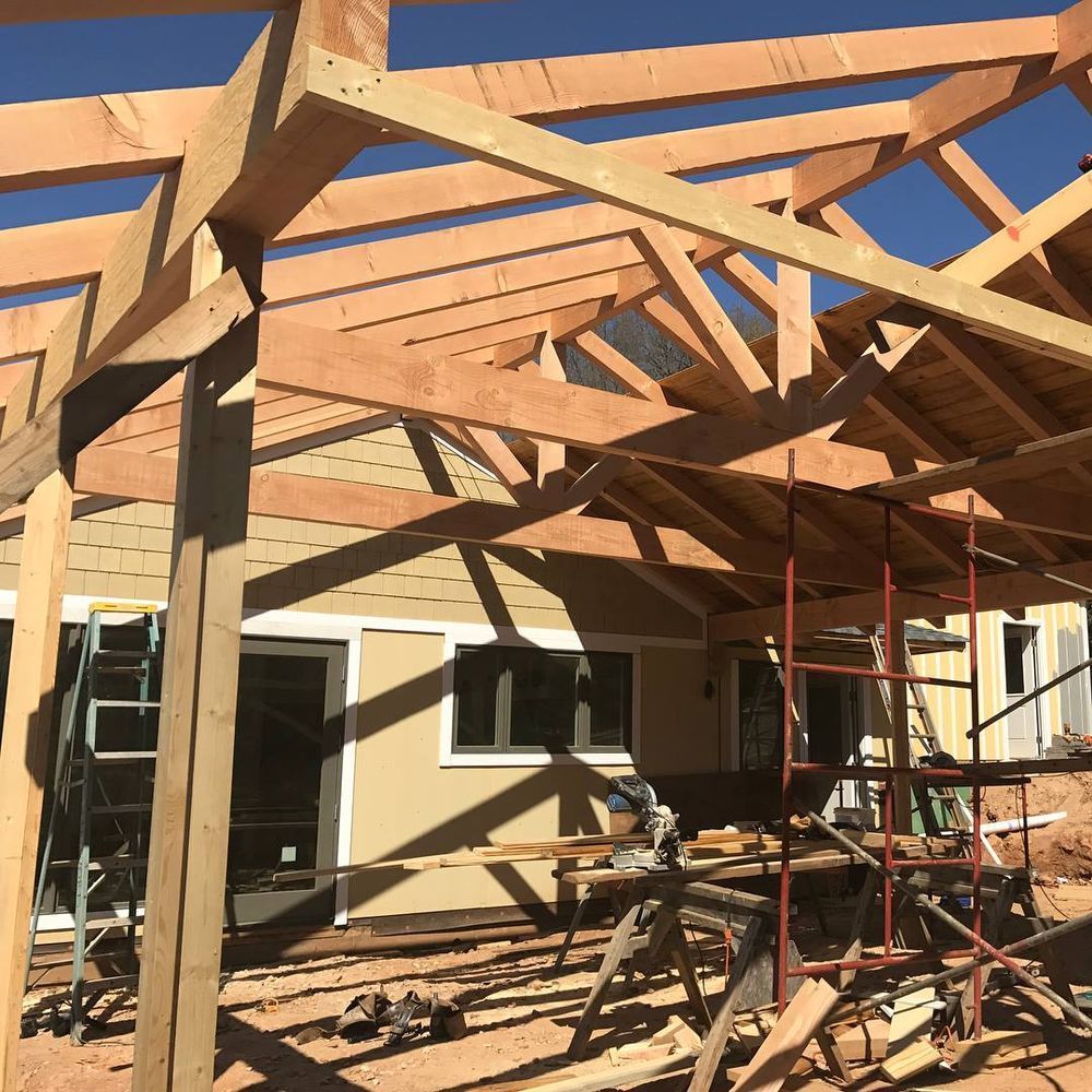 Unfinished house roof framing with exposed wooden beams and scaffolding under a clear sky