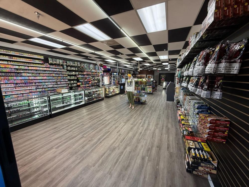 Convenience store aisle with snacks, drinks, and a checkered black-and-white ceiling, viewed from the front.