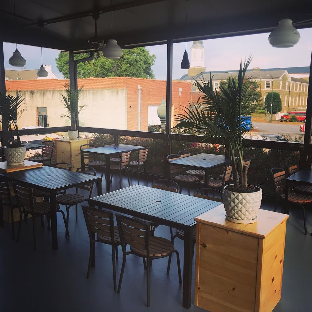 Outdoor café terrace with empty tables, wicker chairs, hanging lights, and potted plants at sunset.