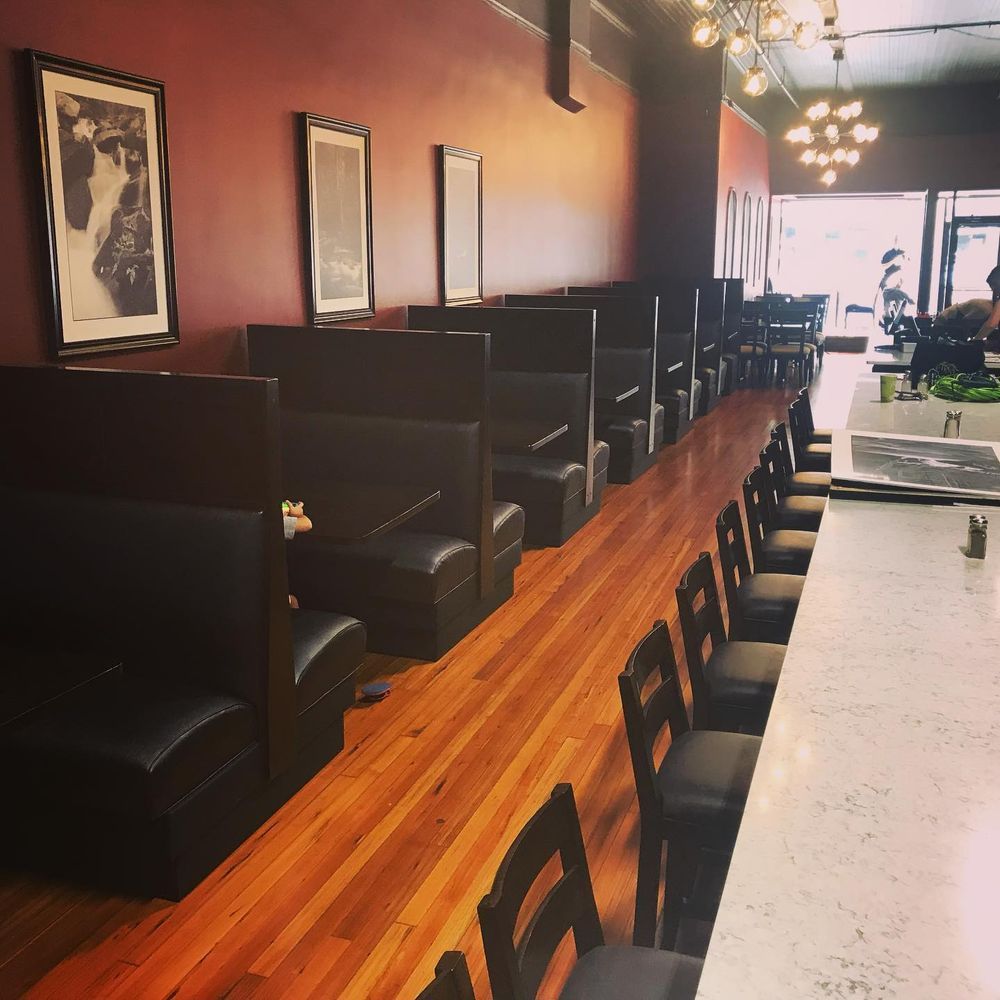 Dim restaurant interior with black booths along a wooden floor and a long white counter.
