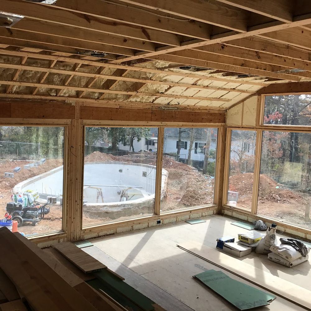 Unfinished sunroom interior with exposed beams, large windows, and construction materials on the floor