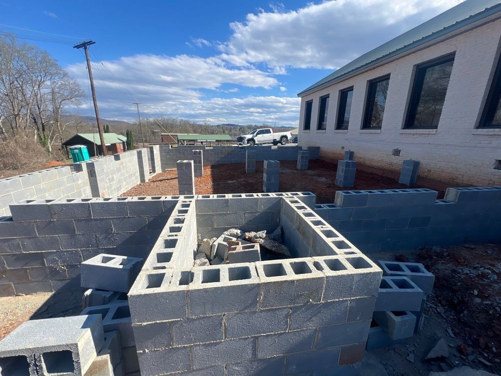Construction site with cinder block foundation beside a building under a blue sky